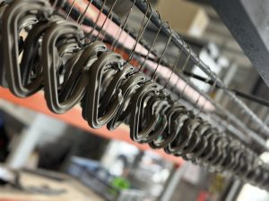A row of metal carabiners hanging on a wire in an industrial or workshop setting.