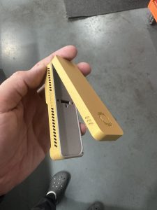 A hand holds an open rectangular gold metal case with ventilation holes and a sun-shaped engraving on the lid.